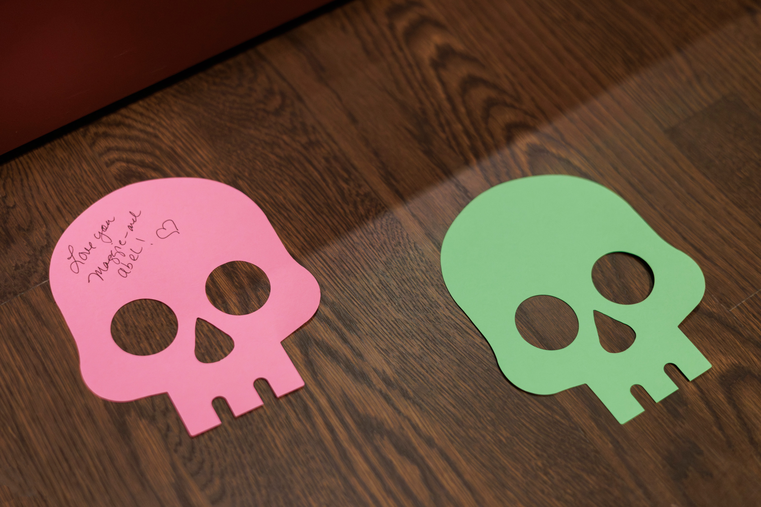 2 paper skulls on the floor. 1 has writing on it that says love you maggie and abel!