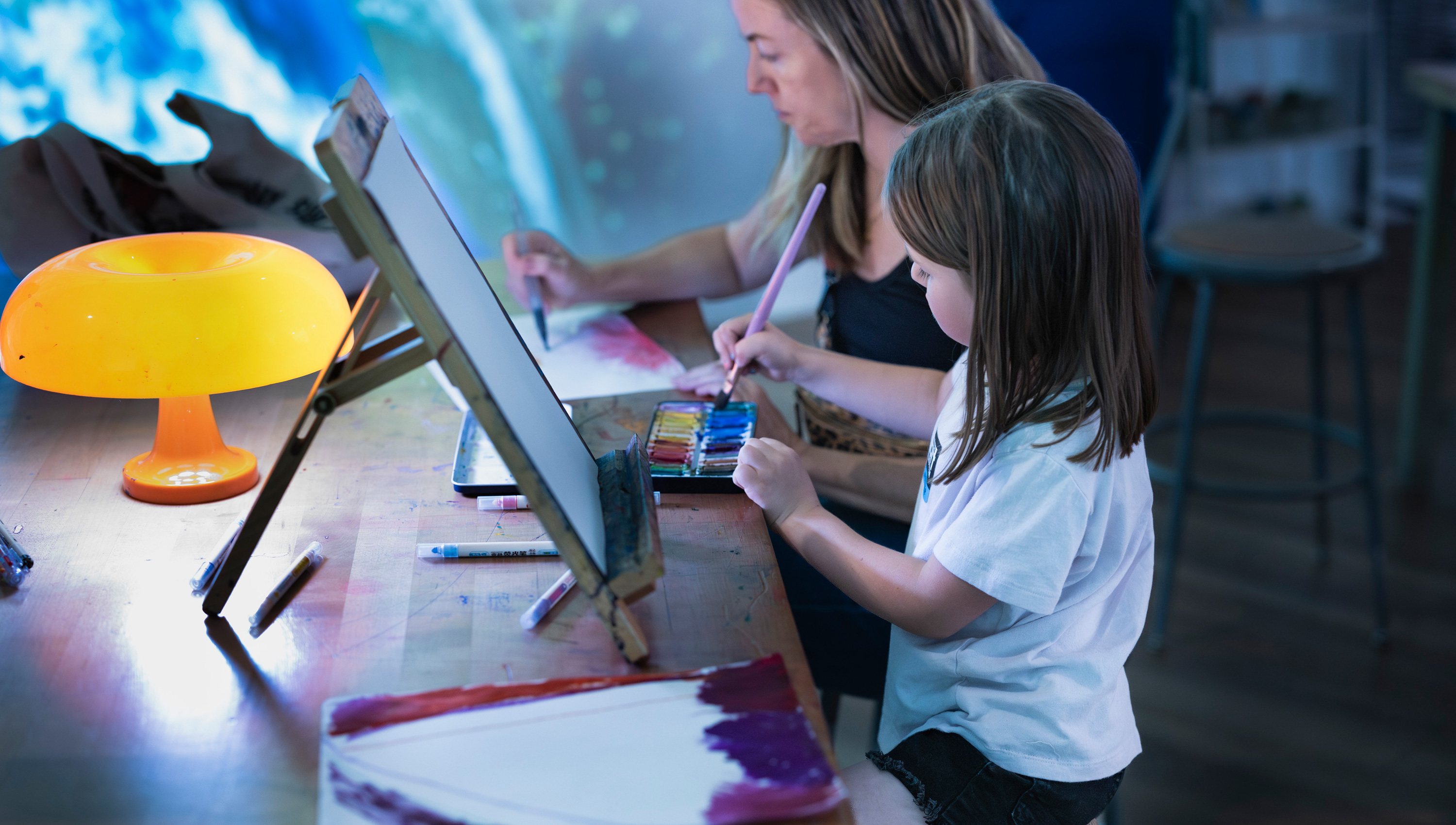 a child and a parent paint side by side in the Cosmic Studio