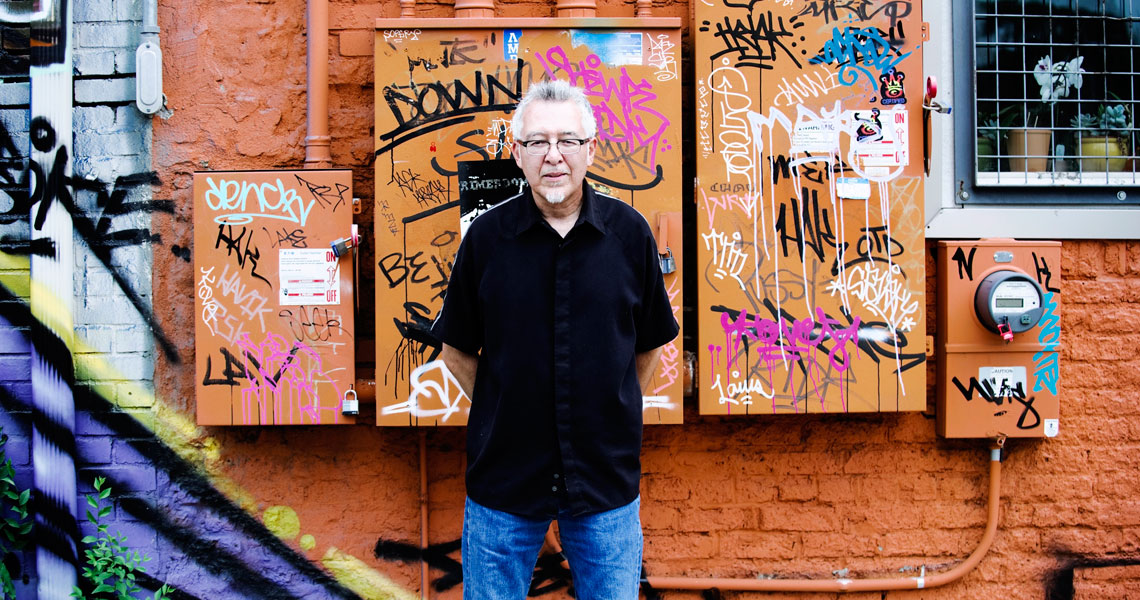 Carlos Fresquez standing in front of a wall of colorful grafitti