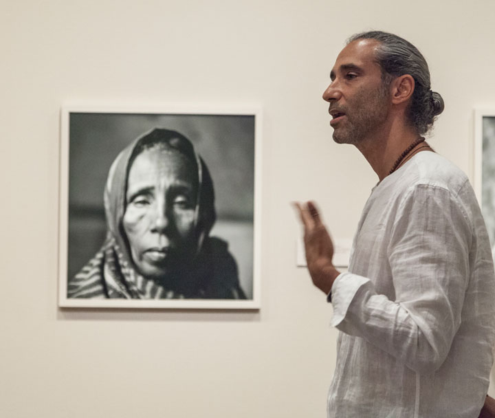 Fazal Sheikh in the gallery in front of a black white photo of a woman