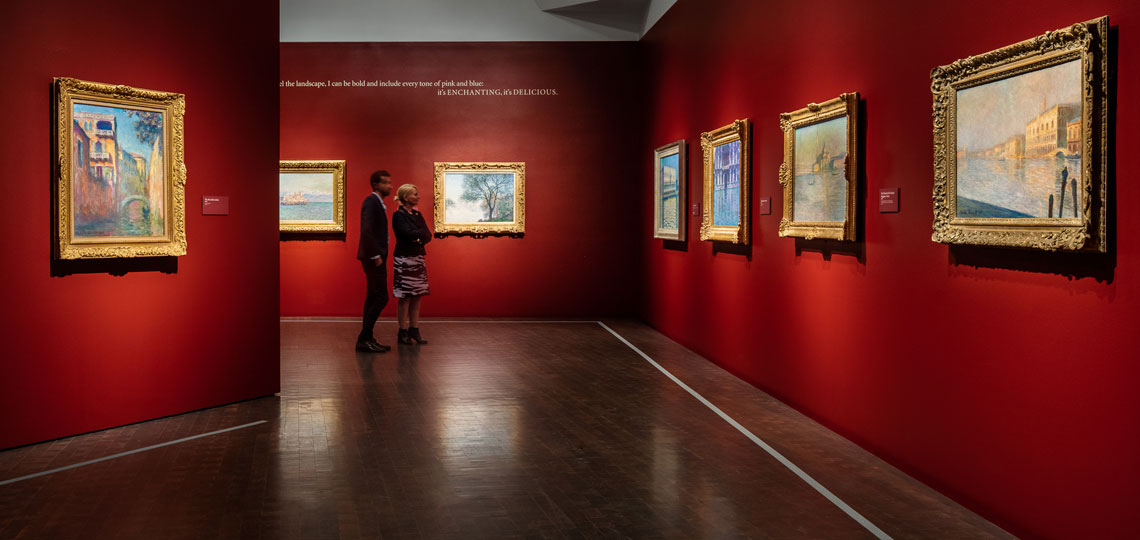 a man and a woman in the Monet exhibition looking at paintings in gold frames