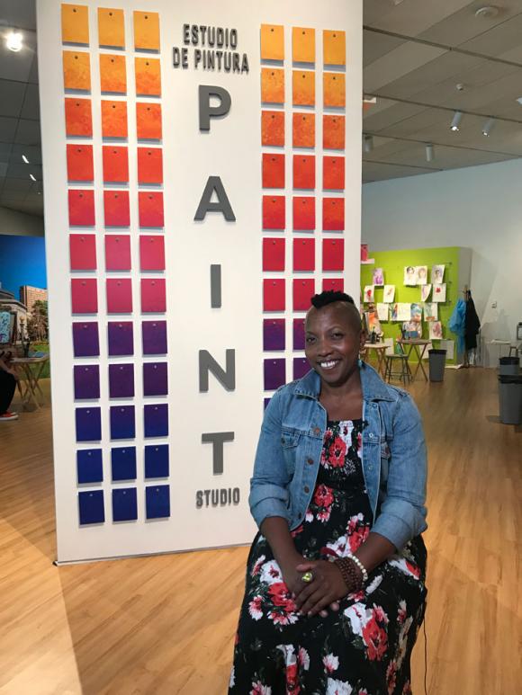 Quana Madison sitting in front of a wall with the words Paint Studio