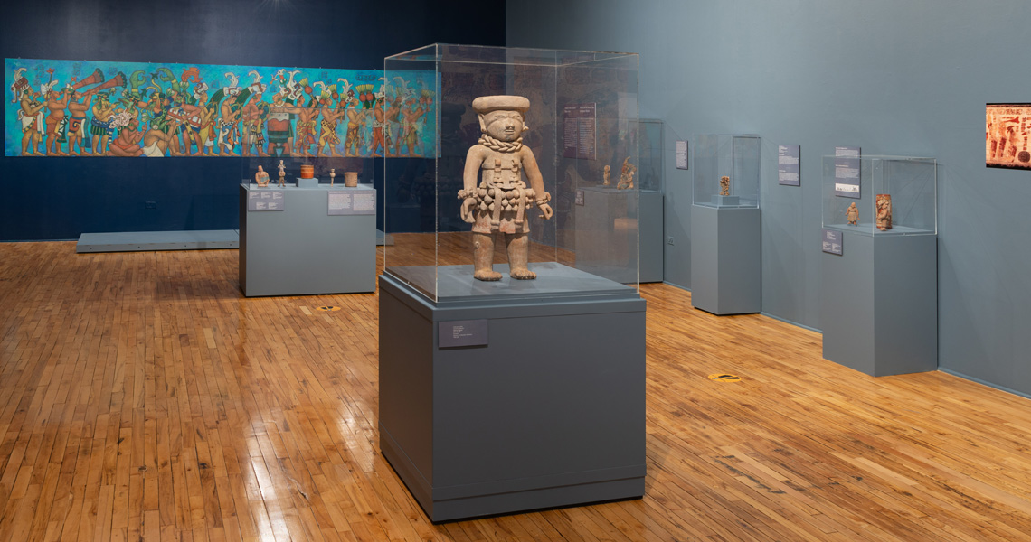 Gallery view of the Rhythm and Ritual exhibition with ancient musical instruments inside glass cases and a painting of ancient musicians on the wall