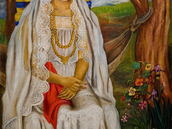 A woman in a white wedding dress sitting with her arms folded and with red roses in her hair