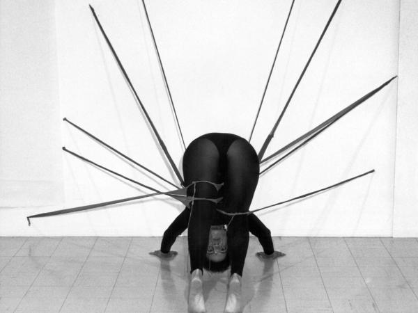 A woman bent over made to look like a sculpture tied to the wall.