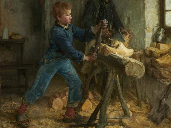 A young boy carving wood as his father supervises.