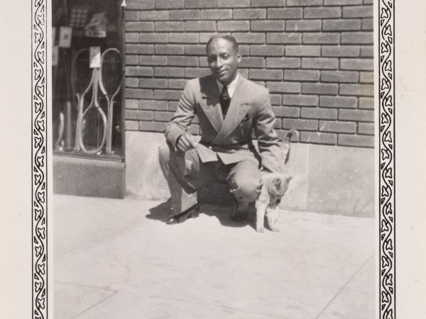 a man squatting down to pet a cat outside in front of a brick wall