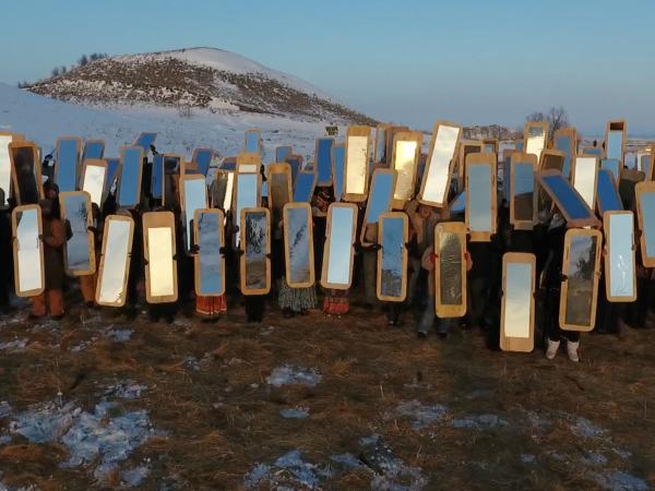 Dozens of people holding up mirrors on a mountainside