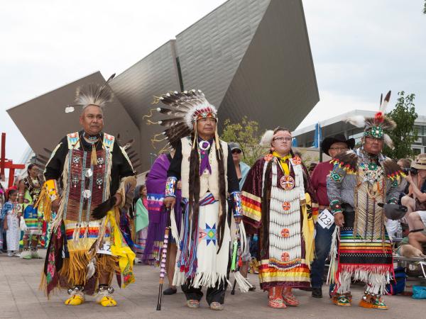 Men and women dressed in traditional Indigenous clothing celebrating Powwoww in front of the museum entrance