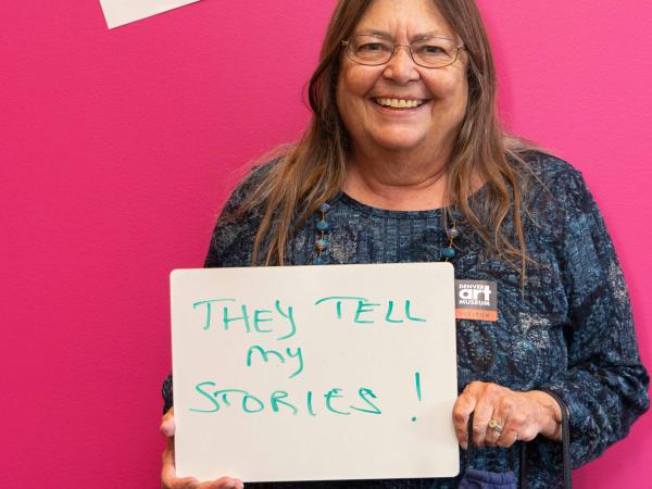 Woman posing with a written sign that says "I take photos because they tell my stories!"