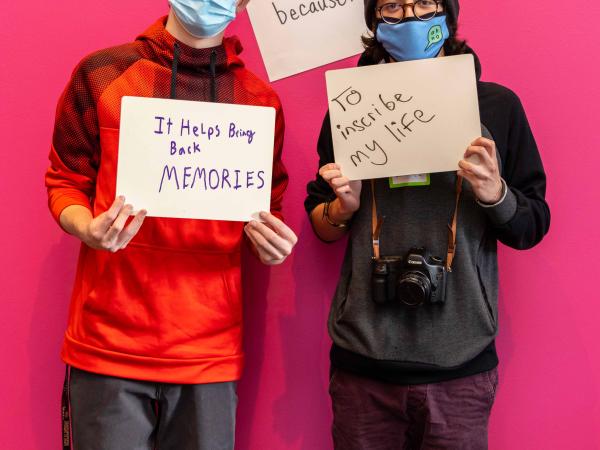 Two teens posing in the exhibition with written signs explaining their reasons why they take photos