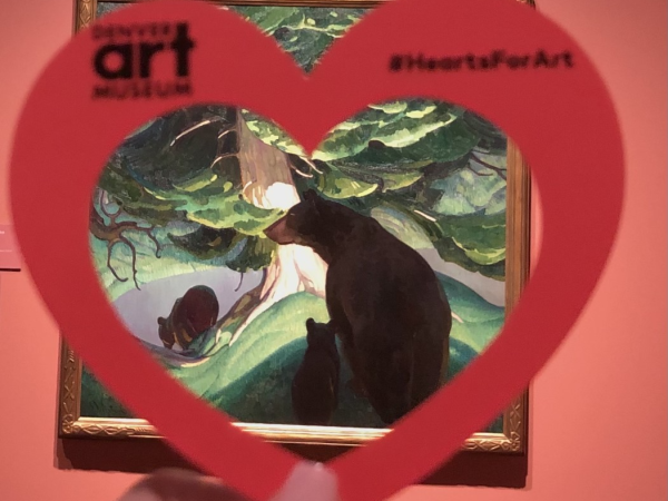 Hand holding a paper heart in front of the artwork "Black Bears" by Herbert Dunton at the Denver Art Museum.