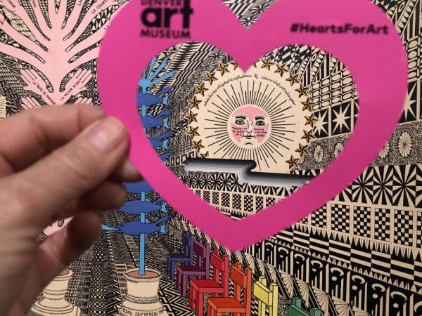 Hand holding a paper heart in front of Pedro Friedeberg's "Kant's Kindergarten."