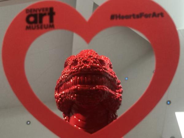 Hand holding a paper heart in front of the statue "Made in China" at the Denver Art Museum.