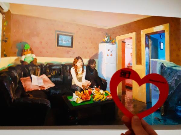 Hand holding a paper heart in front of the artwork, "She—White Collar Worker" by Yu Hong