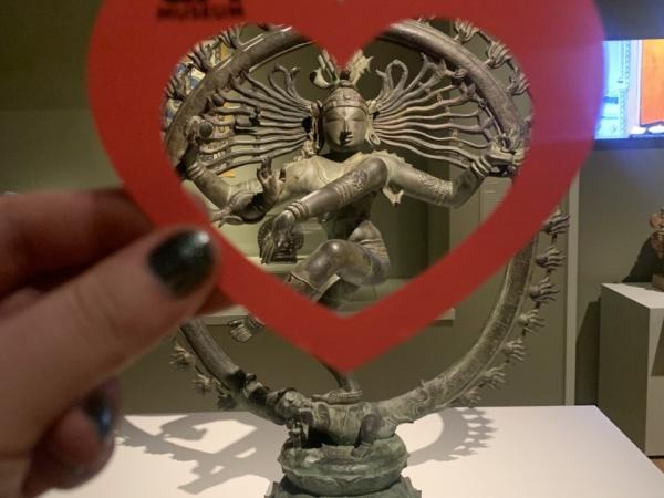Hand holding a paper heart in front of the statue "Shiva Nataraja"