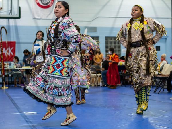 Two women in traditional Indigenous clothing performing for a crowd at Powwow 2021