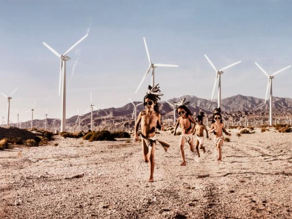 Desert landscape with children running in the foreground and solar windmills in the background