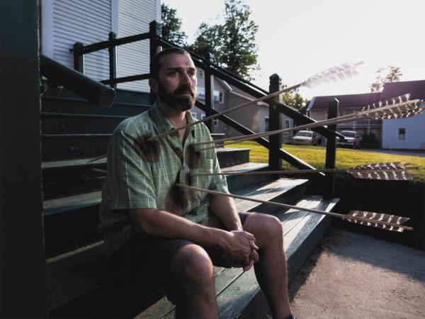 Man sitting on steps with arrows shot through his chest