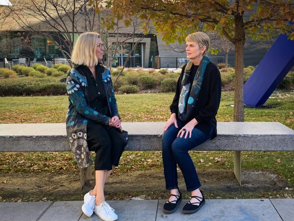 two women sit on a bench outside the museum modeling a duster and a scarf by Betsy Wiersma