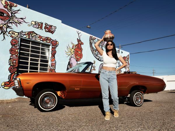 Woman holding a pot over her head, leaning against an oragne convertible car
