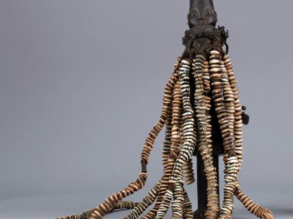 Esu figure with long necklaces of cowrie shells strung on hide straps