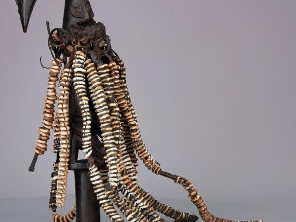 Esu figure from the side showing all the repaired strands of hide and cowrie shells