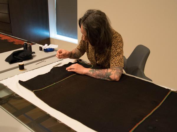 conservator at a table sewing a long brown textile