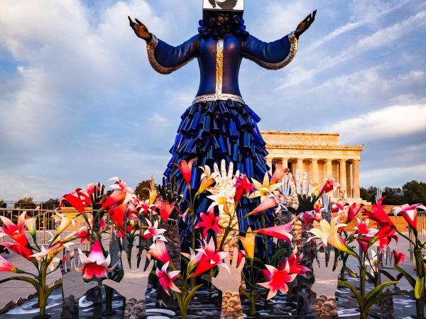 Mixed media installation of a sculpture of a powerful large figure giving a speech to a group of men