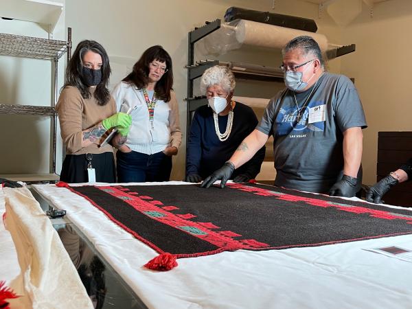 people around a table with a black and red texile. A man points at the fabric