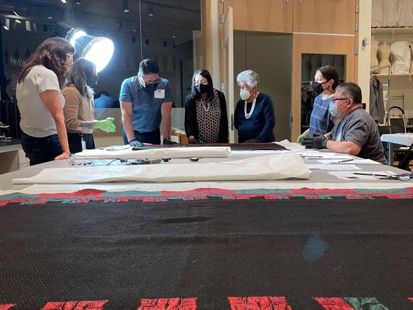 DAM staff and Acoma cultural advisors looking at a large cloth on a table in the textile conservation lab