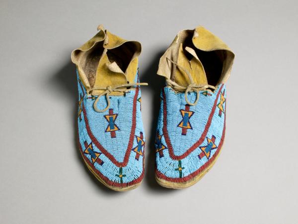 Moccasins made out of leather and beads with a bright blue patterned coloring on the outside