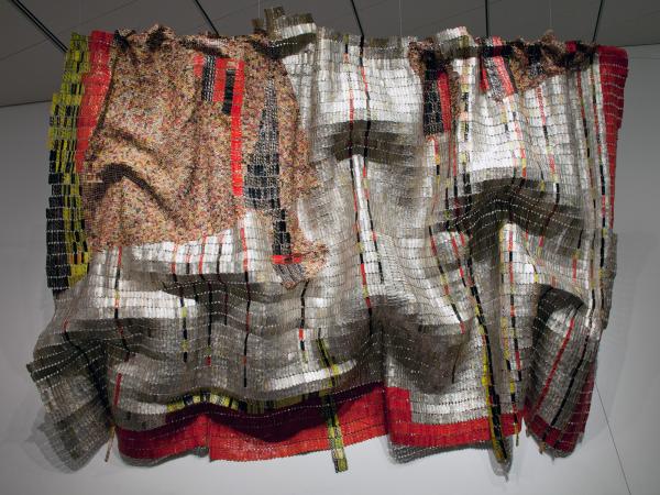 Hanging installation of a large blanket-like tapestry made out of bottle tops and copper wire