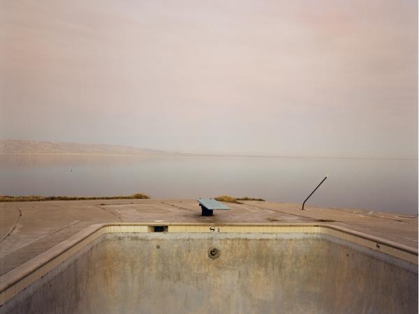 Photograph of a diving board, water, and light grey sky