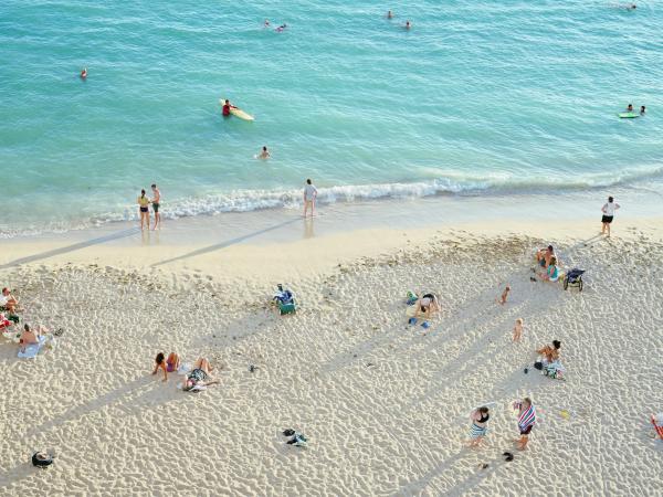Overhead view of people lounging on a beach next to clear blue ocean waters