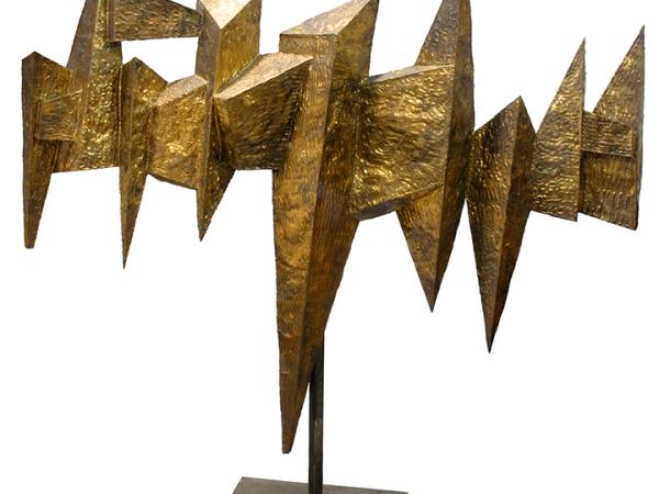 Gold geometrical sculpture resembling a bird with outstretched wings