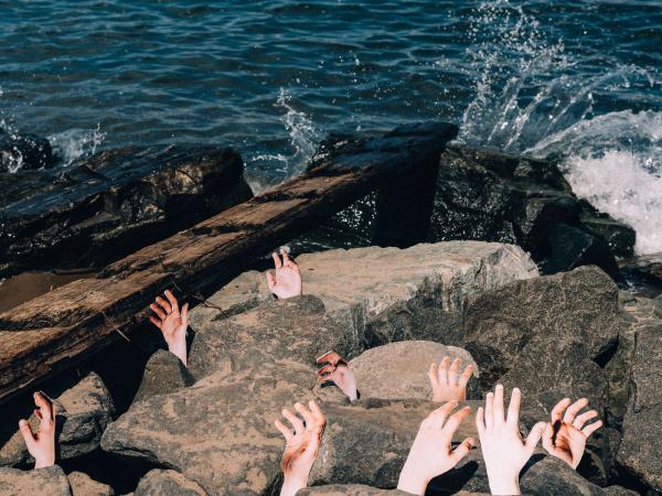 Severed hands rising from the rocks near a beach and body of water