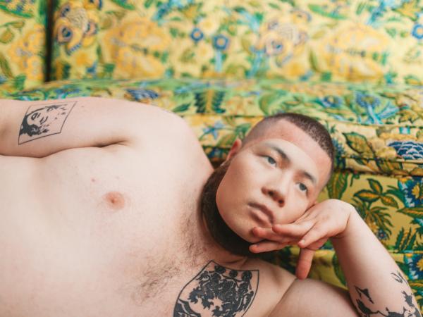 Larger shirtless man resting his head on his hand in a spring field