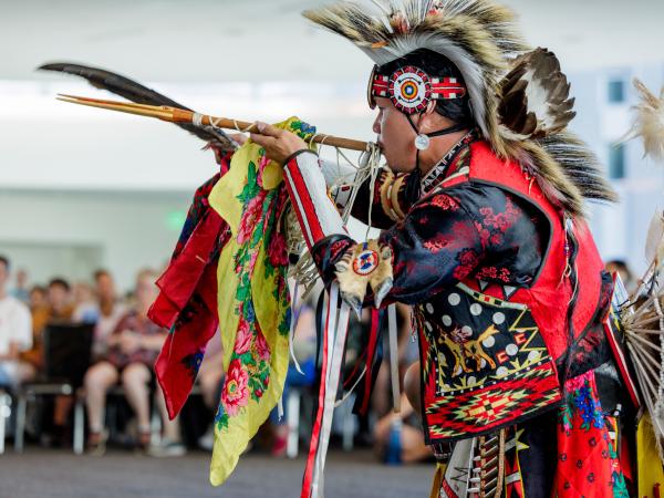 Man performing with a flute while dressed in traditional Native American wear 