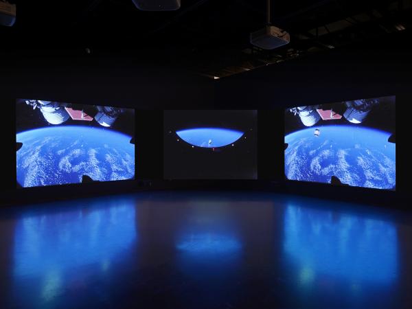 Three large projection screens displaying images of space