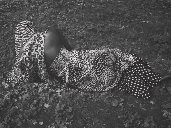 Black woman wearing leopard print clothing lying on the ground facing away from the camera