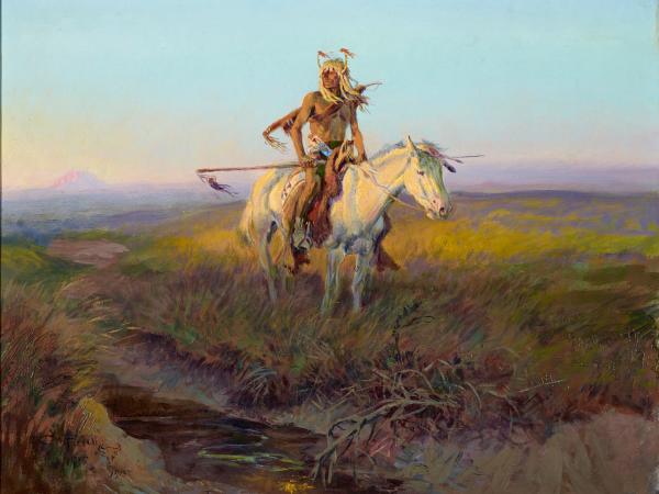 Native American man riding a white horse in the middle of the Western plains