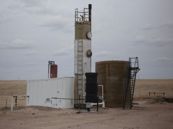 A seemingly abandoned industrial structure stands rusting in the middle of a yellow prarie.