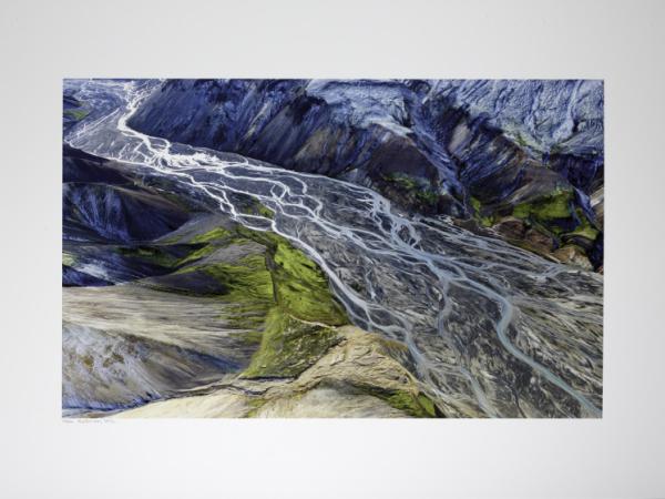 Colorful aerial photo graph of a fertile glacial delta cut between two ridgelines. The lines of the delta frequently branch and rejoin each other evoking the image of a braid.