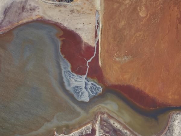 A high altitude photo of the Salt Lake basin where a source of water pours into the basin, creating a delta-like pattern of grey water blending into the brackish brown of the lake.