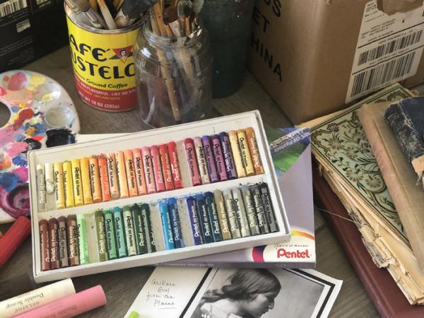 pastels, paint supplies, and black and white photo of an Indigenous woman on a table with other art supplies