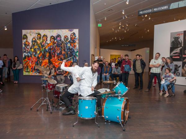 2 men playing drums in the Stampede exhibition with crowd watching at Untitled Final Friday