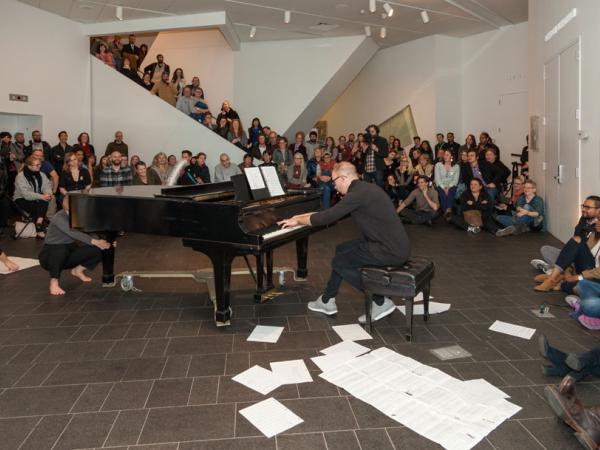 musician at a grand piano surrounded by papers on the floor and a large crowd at Untitled Final Friday