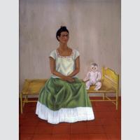 Kahlo sits on a small bed next to a pale, stiff baby doll. Wearing a white top and green skirt, she stares directly out of the frame at the viewer.