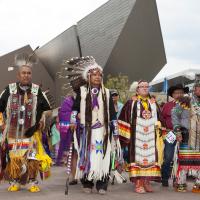 Men and women dressed in traditional Indigenous clothing celebrating Powwoww in front of the museum entrance